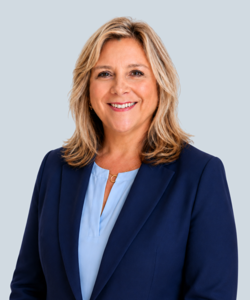 Smiling woman in navy blazer and light blue blouse posing for professional headshot on gray background