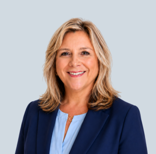 Smiling woman in navy blazer and light blue blouse posing for professional headshot on gray background