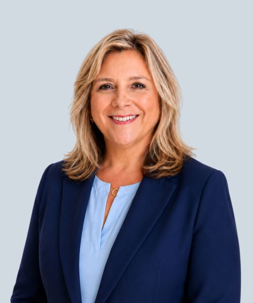 Smiling woman in navy blazer and light blue blouse posing for professional headshot on gray background