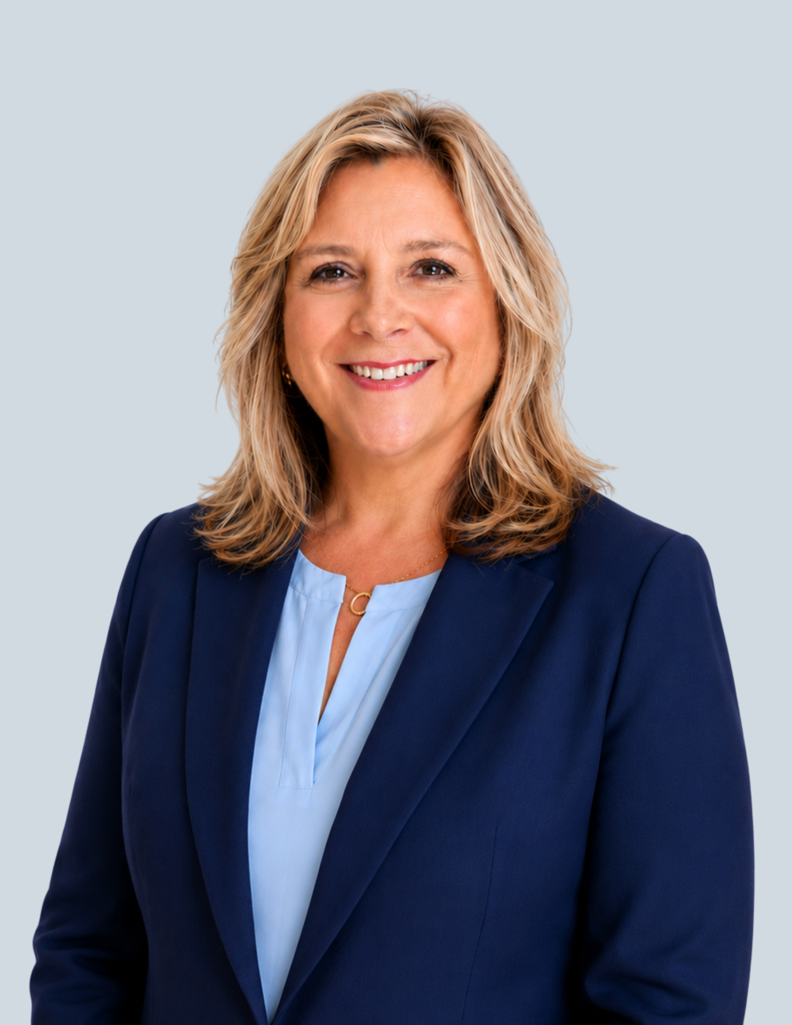 Smiling woman in navy blazer and light blue blouse posing for professional headshot on gray background