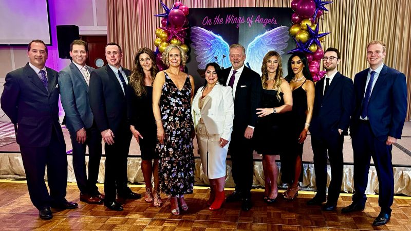 Group of people posing at an event with colorful balloons and wings backdrop.