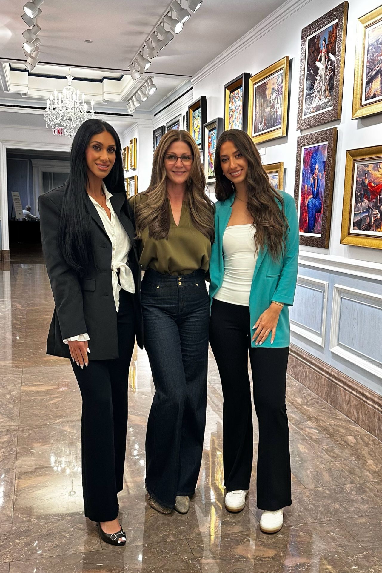 Three women standing together in an art gallery, smiling at the camera.