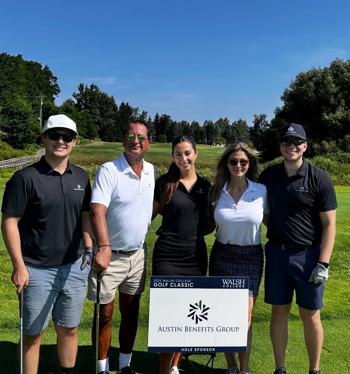 Five people pose by a golf sponsor sign at Walsh College event.